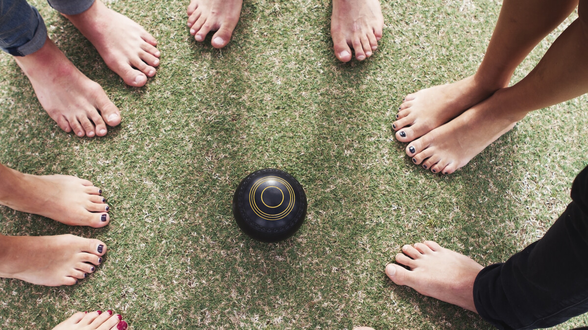 Overhead view of bare feet friends on grass around lawn bowls